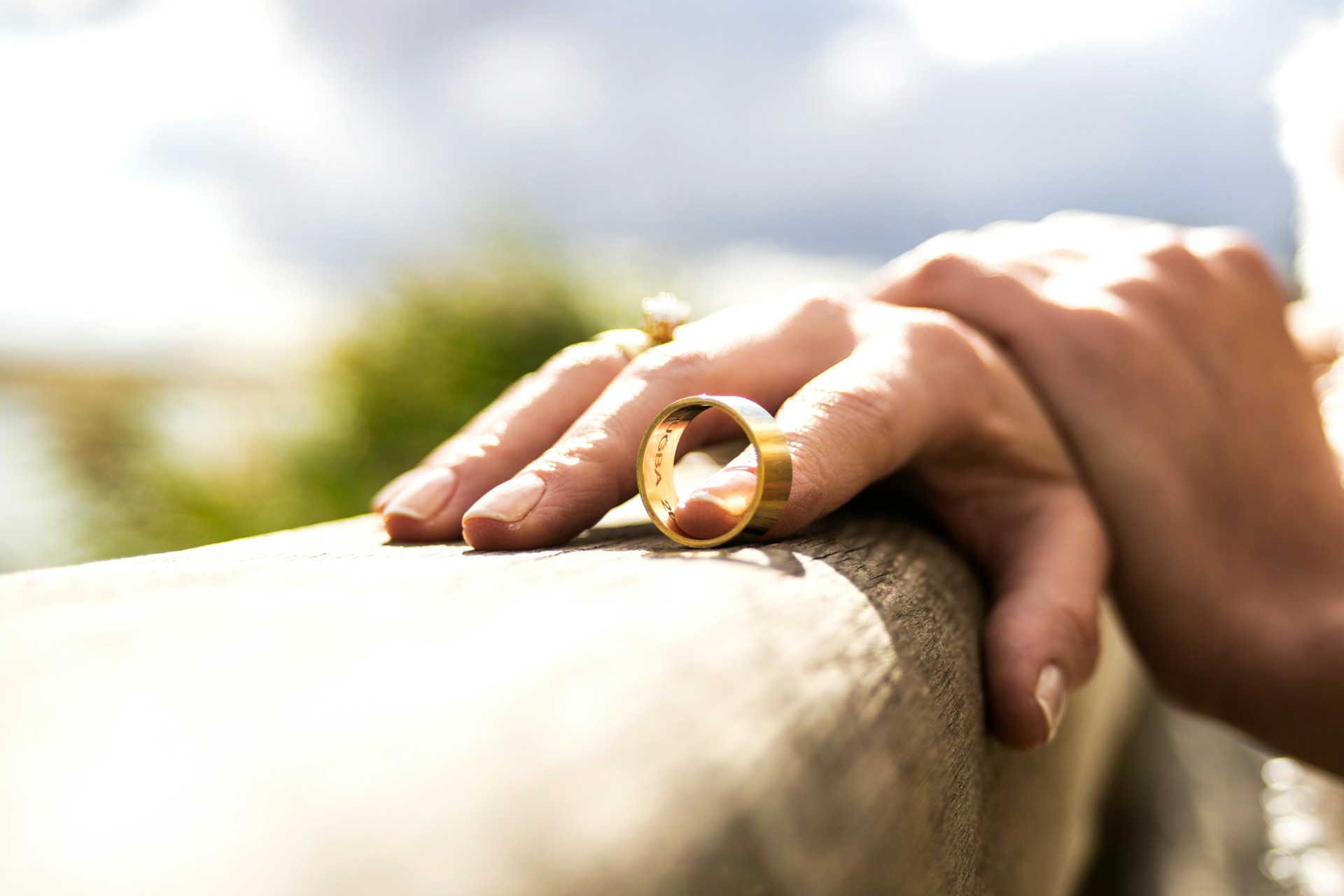 wedding rings resting on a wooden surface, two hands nearby
